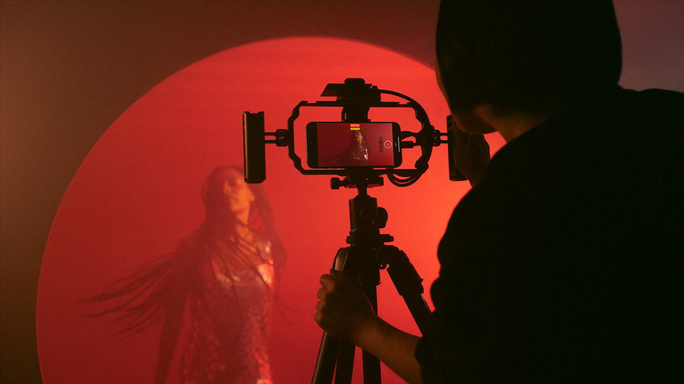 Foto de uma pessoa usando um iPhone com um tripé para gravar um vídeo colorido de uma mulher.
